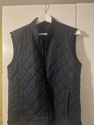 Blå Morris väst  - Snygg och stilig marinblå dunväst från Morris med quiltat mönster och diskret logga på bröstet. Västen har ståkrage, dragkedja framtill och två fickor. Perfekt för lager-på-lager och ger en stilren look. Materialet är lätt och värmande. Nypris: 2000kr. Priset kan diskuteras! 