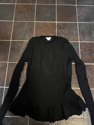 Svart ribbstickad tröja från H&M - Säljer en svart ribbstickad tröja från H&M med lång ärm och rund halsringning. Tröjan har en lätt utsvängd nederkant och är tillverkad i ett mjukt, stretchigt material som sitter snyggt på kroppen. Perfekt för dig som gillar enkel men stilren design.