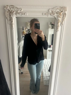 Svart långärmad blus från Saint tropez - Säljer en svart blus från Saint tropez med v-ringning och knappar framtill. Blusen har långärmad design och är tillverkad i ett tunt, lätt material som ger en avslappnad och stilren look. Perfekt att matcha med jeans eller kjol.