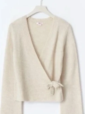 Beige omlottkofta med knytband - Mysig beige stickad omlottkofta med knytband i midjan. Koftan har lång ärm och ribbade muddar. Perfekt för lager på lager och ger en avslappnad men ändå stilren look.