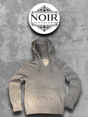 Grå hoodie från Hollister - Snygg grå hoodie från Hollister med klassisk huva och dragsko. Tröjan har en stor magficka och det ikoniska Hollister-logotypen broderad på bröstet. Tillverkad i mjukt material som passar perfekt för en avslappnad stil. 