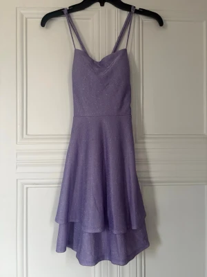 Lila glittrig klänning XS prom/events - Lika kortklänning med glittrigt tyg axelband i kryss. Klänningen har spetsdetalj i ryggen. Perfekt för skolans prom, dans, osv. Den är XS. 