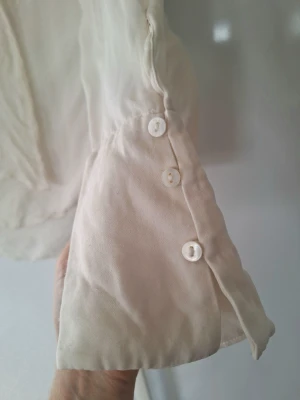 Vit omlottblus från Zara.  - Snygg vit blus i tunt, lätt material med dekorativa knappar vid ärmslutet. Blusen har en feminin, luftig passform. Perfekt att styla med jeans eller kjol för en trendig look. Ber om ursäkt för ostruken.