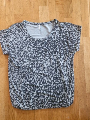 Leopardmönstrad t-shirt från Soyaconcept - Cool t-shirt från Soyaconcept med grå/grönt och svart leopardmönster. Den har korta ärmar och en rund halsringning. Perfekt för dig som gillar att sticka ut med ett djurinspirerat print. Materialet känns mjukt.
