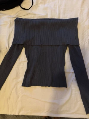 Mörkblå offshoulder ribbad topp - Snygg mörkblå ribbad topp med offshoulder-design och långa ärmar. Perfekt för dig som vill ha en stilren och trendig look. Materialet är stretchigt och följsamt, vilket gör att toppen sitter tight och bekvämt.