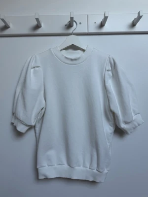 Vit  topp med puffärm i sweatshirt tyg - Säljer en stilren vit topp med puffärmar och ribbade muddar vid hals, ärmslut och nederkant i sweatshirt tyg. Toppen har en relaxed fit och är tillverkad i mjuk bomull, perfekt för en clean och trendig look.