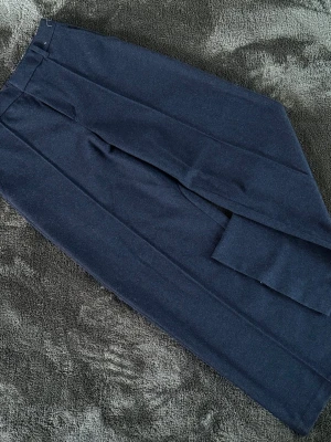 Mörkgrå kostymbyxor från Uniqlo - Storlek 30-31 Snygga mörkblå kostymbyxor från Uniqlo med klassisk rak passform och pressveck. Byxorna är tillverkade i ett mjukt material med återvunna fibrer och har diskreta fickor. Perfekta för en stilren look. 