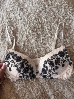 Vit spets-bh med svart blommönster - Säljer en vit spets bh från intimissimi som inte kommit till användning, den har däremot en liten fläck på insidan (se sista bild) de kan va så att den går bort i tvätt har ej testat men den syns inte vid använinding💕
