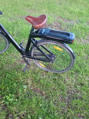 Svart elcykel Asaklitt med brunt sadel - Säljer en svart elcykel från Asaklitt med brunt sadel och batteri placerat bak på pakethållaren. Cykeln har reflexer på hjulen, stänkskärmar och robust ram. Perfekt för dig som vill ha smidig och miljövänlig transport. Laddaren följer ej med! 