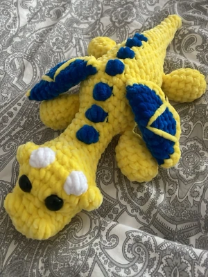Gul och blå virkad drake - Unik handgjord drake i mjukt, tjockt garn. Draken är gul med blå detaljer på ryggen och vingarna samt vita horn på huvudet. Svarta ögon i plast. Virkad av mig. 