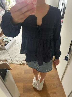 Mörkblå blus med knytning - Snygg mörkblå blus med v-ringning och knytning framtill. Blusen har långa ärmar med resår vid ärmslut och ett luftigt, flowy tyg som ger en avslappnad känsla. Perfekt att styla med jeans eller kjol för en trendig look.
