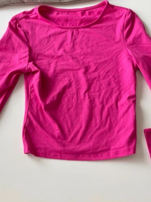 Rosa långärmad topp i bomull - En enkel och snygg långärmad topp i stark rosa färg. Tillverkad i mjuk bomull med rund halsringning och normal passform. Perfekt att styla med jeans eller kjol för en färgstark look.