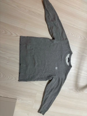 Grå sweatshirt från Acne Studios - Säljer en stilren grå sweatshirt från Acne Studios. Tröjan har rund halsringning, långa ärmar och en liten patch framtill. Tillverkad i mjukt bomullsmaterial med borstad insida för extra komfort. Perfekt för en avslappnad och trendig look.