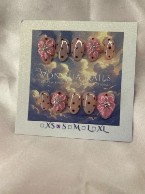 RosyDot (S);Short Almond - Unika handgjorda press-on naglar i rosa och nude toner med bruna prickar och handgjorda blommor som detaljer. Några naglar har handgjorda 3D-blommor och små silver pärlor för extra wow-effekt. Perfekt för dig som vill ha något kreativt och trendigt på naglarna.S: 15 mm, 11,5 mm, 12 mm, 11 mm, 9 mm 