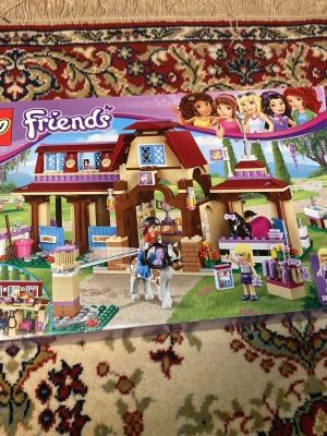 LEGO Friends Häststall 41126 - Säljer ett LEGO Friends set med häststall, hästar och flera minifigurer. Setet har detaljer som sadlar, borstar och stallinredning. Färgerna är lila, röd, beige och brunt. Perfekt för dig som gillar hästar och att bygga med LEGO.