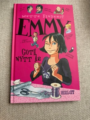 Emmy: Goth nytt år av Mette Finderup - En ungdomsroman med hård pärm i stark rosa färg, skriven av Mette Finderup. Boken har tecknade illustrationer på omslaget och handlar om Emmy och hennes vardag, vänskap och utmaningar. Perfekt för dig som gillar humor och tonårsliv.
