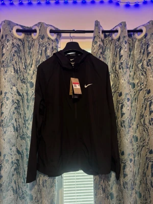 Svart Nike träningsset med huva och byxa  - Snyggt svart träningsset från Nike med långärmad hoodie och matchande byxor. Båda plaggen har den klassiska vita Nike-loggan. Hoodien har dragkedja och huva, byxorna har dragsko i midjan. Perfekt för gymmet eller löprundan.