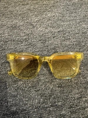 Chimi 04 fyrkantiga solglasögon - Snygga solglasögon med transparent gul båge och fyrkantig form. Glasen är tonade i gult och ger en cool retrovibe. Perfekta för dig som vill sticka ut och addera färg till din stil. Kommer med vit hård förvaringsbox och tygpåse. Chimi 04 gula.