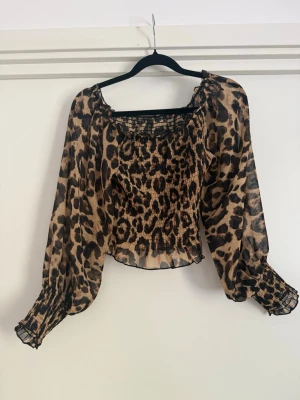 Leopardmönstrad transparent blus - Trendig blus med leopardmönster i beige och svart. Modellen har långa, puffiga ärmar med smock vid handlederna och en rak, något kortare passform. Tillverkad i ett tunt, transparent material som ger en luftig känsla. Perfekt för dig som vill sticka ut.