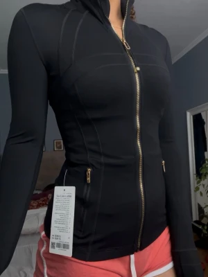 Svart gold zipper define jacket - Helt ny lululemon black gold zipper define jacket i nulu. Har ej kommit till användning endast testat, storlek 4 passar XS-S