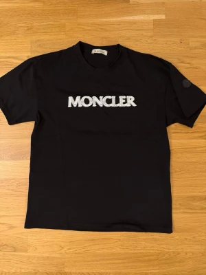 Svart Moncler t-shirt med logga - Helt oanvänd. Nfs loga som går att scanna genom att lägga mobilen nära. Även qr kod på insidan. Stl S men passar även som M då den är lite oversize!