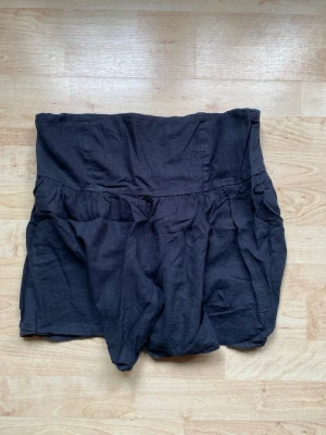 Svart bandeau tubtopp i bomull - Svart axelbandslös tubtopp i mjuk bomull med bred smock baktill för skön passform. Toppen har en loose och flowy siluett med lätt rynkade detaljer som ger en avslappnad vibe. Perfekt för dig som gillar enkel och stilren design.