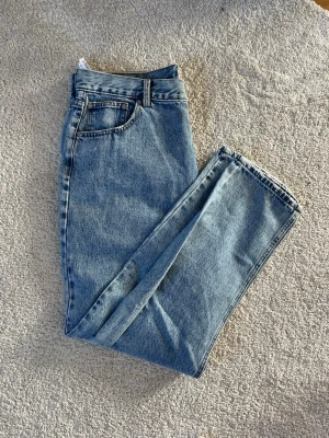 Blå raka jeans från Pull&Bear - Säljer ett par klassiska blå jeans från Pull&Bear i rak modell. Jeansen har fem fickor, bälteshällor och är tillverkade i ett slitstarkt denimtyg. Perfekta för dig som gillar en tidlös och avslappnad stil.