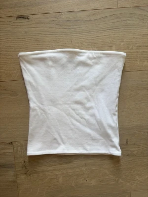 Vit bandeau tubtopp från BikBok xs  - Säljer en enkel och stilren vit bandeau tubtopp från BikBok. Toppen är ärmlös och axelbandslös, gjord i mjuk bomull som sitter skönt mot huden. Perfekt att styla till jeans eller kjol för en clean look. Storlek Xs