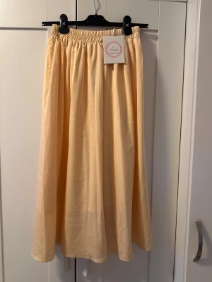 Ljusgul långkjol med resårmidja - Säljer en ljusgul långkjol med resår i midjan. Kjolen har en enkel och flowy design som ger en avslappnad känsla. Perfekt för dig som gillar stilrena plagg med mycket rörelse. Materialet känns lätt och mjukt mot huden. Kjolen är som midikjol.