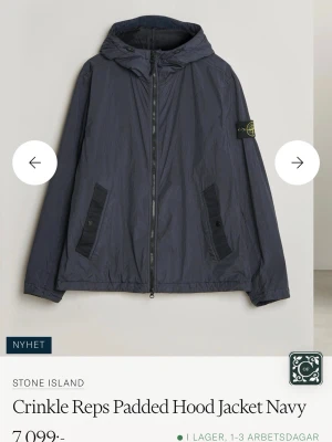 Marinblå vindjacka från Stone Island - Snygg marinblå vindjacka från Stone Island med huva och dragkedja framtill. Jackan har två snedställda fickor med svarta detaljer och den ikoniska Stone Island-loggan på vänster ärm. Tillverkad i lätt, krinklat material som ger en cool look. Bra skick använd ett fåtal gånger kvitto från care of carl finns digitalt