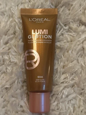 L'Oréal Lumi Glotion 904 Deep Glow - L'Oréal Lumi Glotion i nyansen 904 Deep Glow är en naturligt lystergivande glow enhancer i en brun plasttub med roséguldfärgat lock. Produkten ger huden en fräsch och strålande finish och kan användas som highlighter eller blandas med foundation för extra glow.