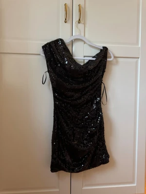 Svart glittrig kort klänning - Snygg svart kort one shoulder klänning täckt med glittriga paljetter.