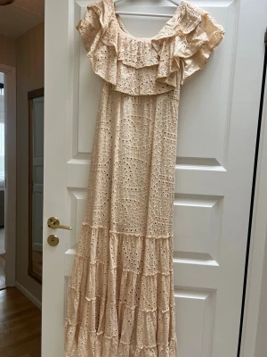 Beige långklänning  - Romantisk beige långklänning med broderade detaljer och volang vid axlarna. Klänningen har en luftig passform, rund halsringning och är ärmlös. Perfekt för sommarens alla tillfällen. Ny pris 700kr
