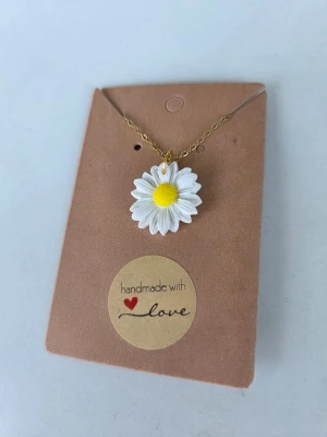 Handgjort halsband med prästkrage i polymerlera - Unikt halsband med en handgjord prästkrage i vit och gul polymerlera. Hängsmycket har en detaljerad blomform och sitter på en tunn guldfärgad kedja. Kedjan är reglerbar upp till 45 cm. 