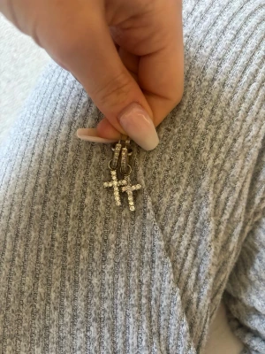 Korsörhängen med pärlor - Säljer ett par snygga örhängen i form av kors, dekorerade med små vita pärlor. Örhängena har en silvrig metallbas och ger ett glittrigt intryck. Perfekta för dig som gillar statement-smycken med lite edge.