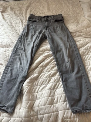 Grå raka jeans från Replay - Säljer ett par grå jeans från Replay med rak passform och klassisk femficksdesign. Jeansen har en diskret tvättad look och är tillverkade i ett mjukt denimtyg som känns bekvämt. Perfekta för dig som gillar en clean och enkel stil.
