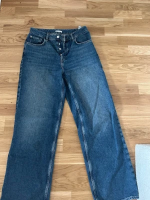 Blåa raka jeans med knappar - Säljer ett par blåa jeans med raka ben och hög midja. Jeansen har knappgylf och klassiska fem fickor. Formar kroppen jättefint