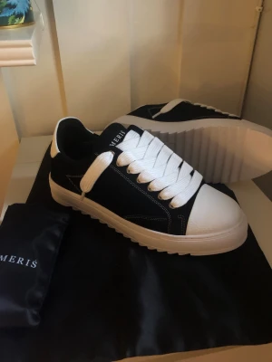 Svarta och vita sneakers från Meris - Stilrena sneakers från Meris i svart och vitt med breda vita skosnören och kraftig vit sula. Ovandelen är i svart material med vita detaljer och tåpartiet är i vitt med textur. Klassisk låg modell som passar till många olika outfits.