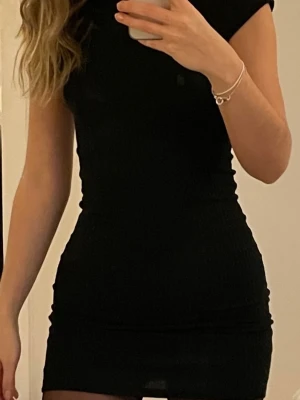 Svart tight kortklänning - Säljer en svart, tight kortklänning med korta ärmar. Klänningen har en enkel och stilren design som framhäver figuren. Perfekt för dig som gillar minimalistisk stil och vill ha en klassisk svart klänning i garderoben.