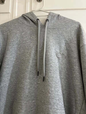 Grå hoodie från CD med broderad logga - Snygg grå hoodie från CD med broderad logga på bröstet. Hoodien har huva med dragsko och en klassisk känguruficka framtill. Tillverkad i mjukt sweatshirtmaterial som är perfekt för chill dagar. Långa ärmar och ribbade muddar för extra komfort.