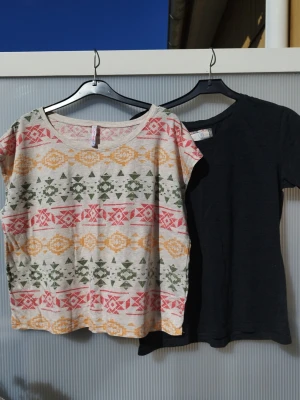 Två t-shirts, en mönstrad och en helgrå  - Säljer två t-shirts: en med färgglatt geometriskt mönster i grönt, gult och rött på beige botten, samt en enkel grå t-shirt. Båda har rund hals och korta ärmar. Perfekta till vardags och lätta att matcha med jeans eller shorts. Båda är i storlek M. Den ena från Primark den andra köpt på NewYorker.