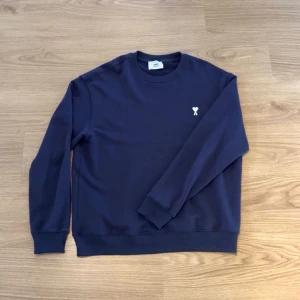Vintage blå/lila - En stilren mörklila sweatshirt med rund hals och en liten vit broderad detalj på bröstet. Tröjan har långa ärmar, ribbade muddar och en avslappnad passform. Perfekt för en casual och trendig look.