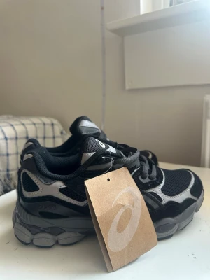 asics new gel nyc - Snygga sneakers från Asics i svart och grått med meshpaneler och detaljer i mocka. Skorna har en chunky sula och klassisk Asics-logga på sidan. Perfekta för dig som gillar sportig och trendig stil.