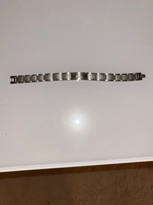 Lacoste armband - Snyggt armband i silverfärgad metall från Lacoste med den klassiska krokodilloggan ingraverad på mitten. Länkarna har en cool rutstruktur som ger en modern och stilren känsla. Perfekt accessoar för dig som gillar sportig och trendig stil. 