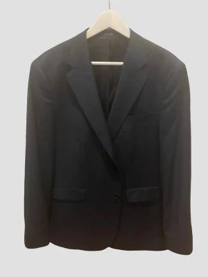 Marinblå klassisk kavaj (56) - Stilren marinblå kavaj med två framfickor och en bröstficka. Klassisk passform med smala slag och enkelknäppning. Perfekt för dig som vill ha en tidlös och snygg look. Materialet känns slätt och elegant.
