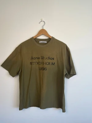 Olivgrön Acne Studios t-shirt - Säljer en olivgrön t-shirt från Acne Studios med tryck på bröstet där det står 'Acne Studios STOCKHOLM 1996'. Klassisk rund hals och korta ärmar. Perfekt för dig som gillar minimalistisk och stilren design. Storlek small, nyskick. 