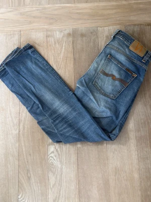 Blå Nudie Jeans Grim Tim - Säljer ett par Grim Tim med sjukt snygg tvätt. Jeansen har fem fickor, normal passform och är tillverkade i bomull. Perfekta för dig som gillar en avslappnad men ändå stilren look. ”Worn in Broken” färg. W32 L31