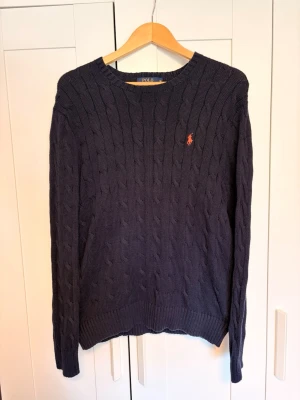 Polo Ralph Lauren kabelstickad tröja – marinblå – strl M - Klassisk cable knit från Ralph Lauren i djup marinblå. 100% bomull, rundringad med det ikoniska ponnyt broderat på bröstet. Sitter snyggt - inte för oversized, inte för tajt. Perfekt för kyligare dagar under sommaren eller kvallar Skriv vid frågor!    Pris ej hugget i sten!