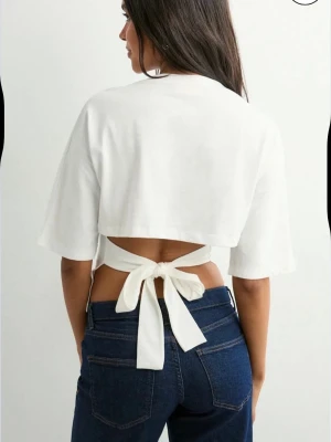 Fin topp med knyt i ryggen - Stilren vit topp med vida korta ärmar och snygg knytning i ryggen. Toppen har en enkel och stilren design som passar perfekt till jeans eller kjol. Tillverkad i mjukt bomullsmaterial för en bekväm känsla.