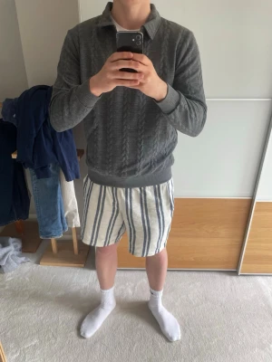 Grå kabelstickad tröja med halvzip - Helt ny schysst grå kabelstickad tröja med halvzip och krage. Tröjan har långa ärmar och ribbade muddar vid ärmslut och nederkant. Perfekt för dig som gillar en klassisk men avslappnad stil och passar perfekt nu mot sommarkvällar